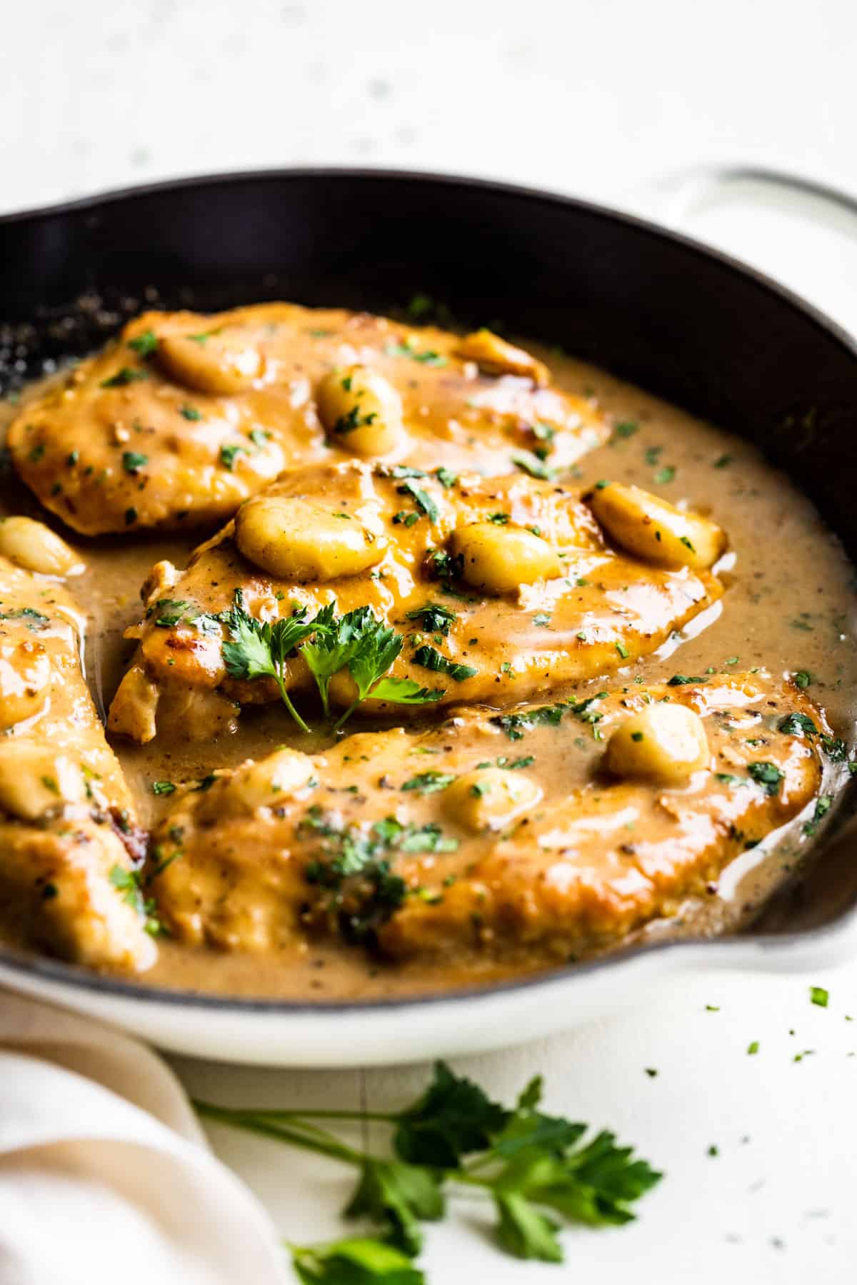 Creamy Garlic Chicken in a white skillet sprinkled with chopped parsley.