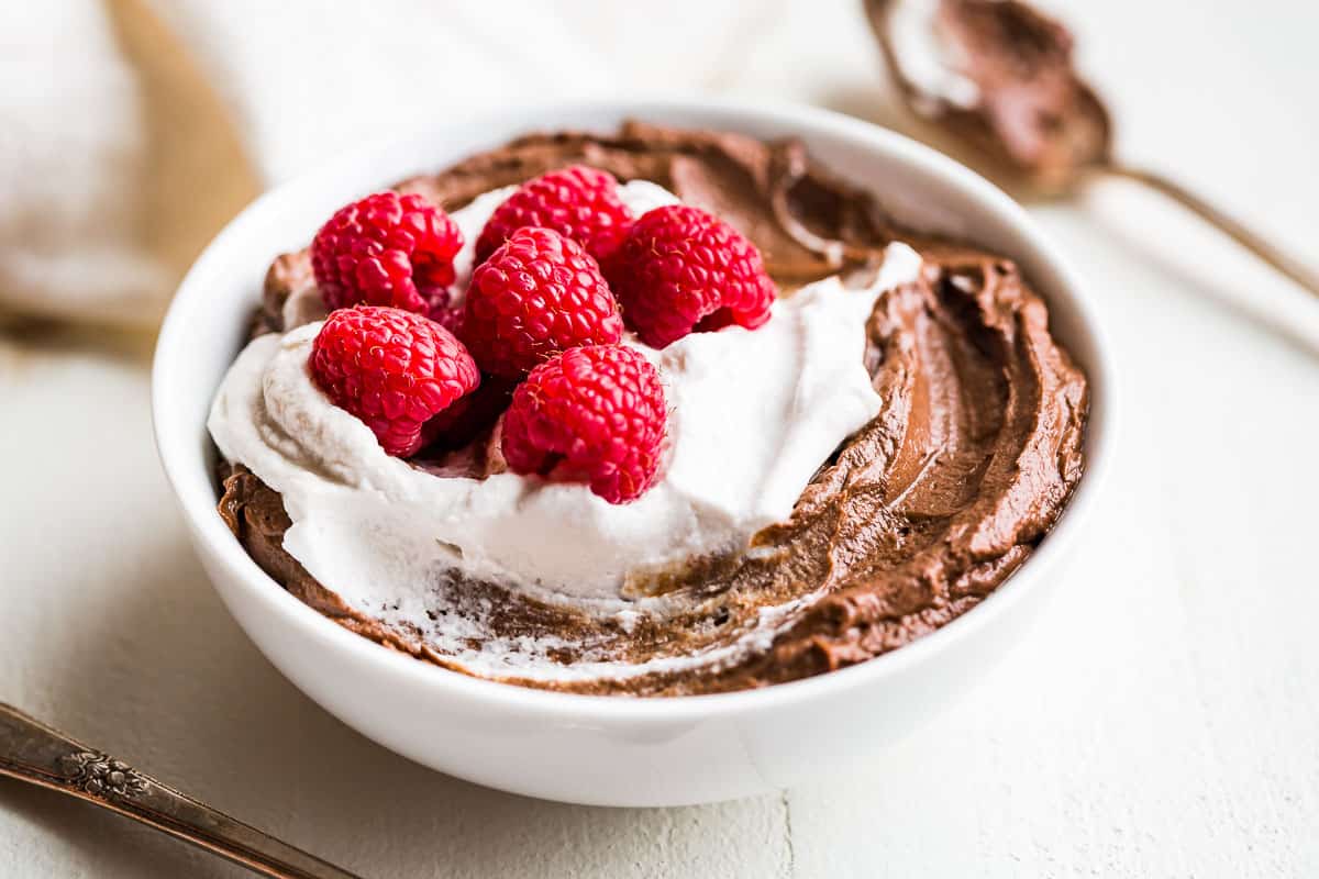 Finished Avocado Chocolate Mousse in a white bowl topped with whipped cream and raspberries.