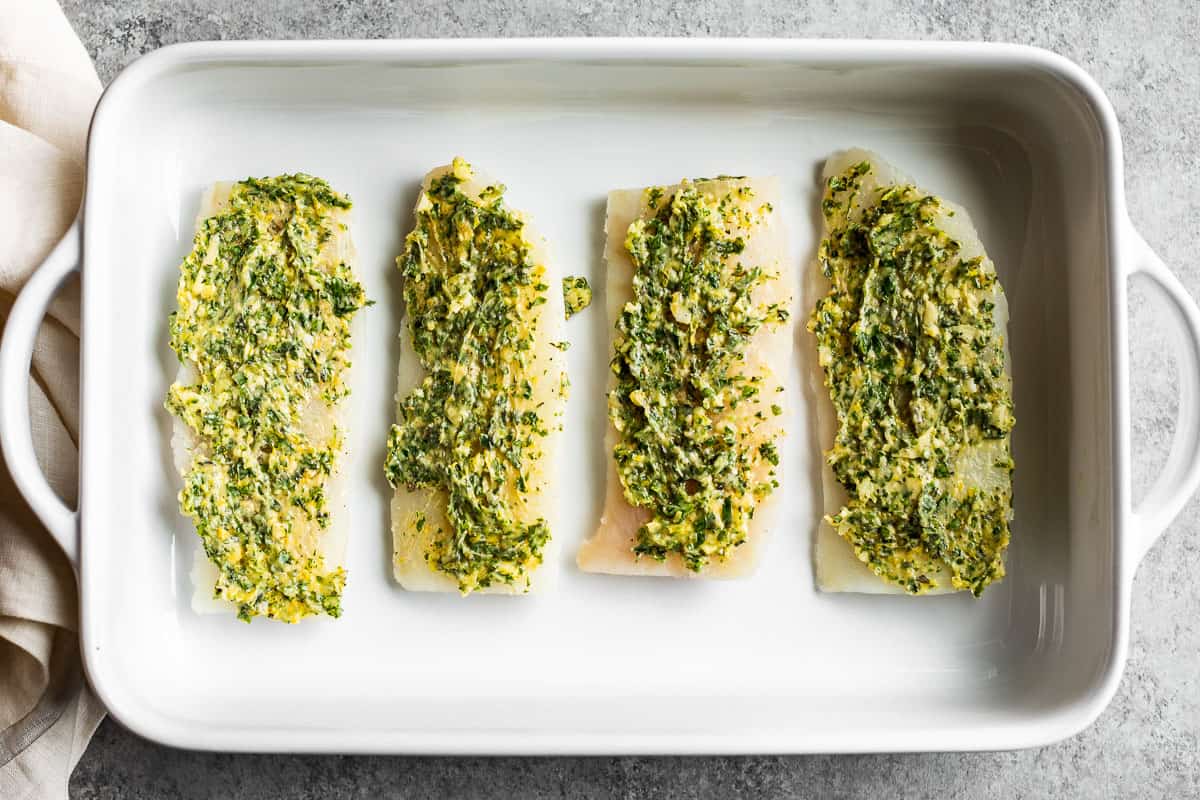 Pieces of cod placed in a baking dish with the herbed butter spread over the tops.