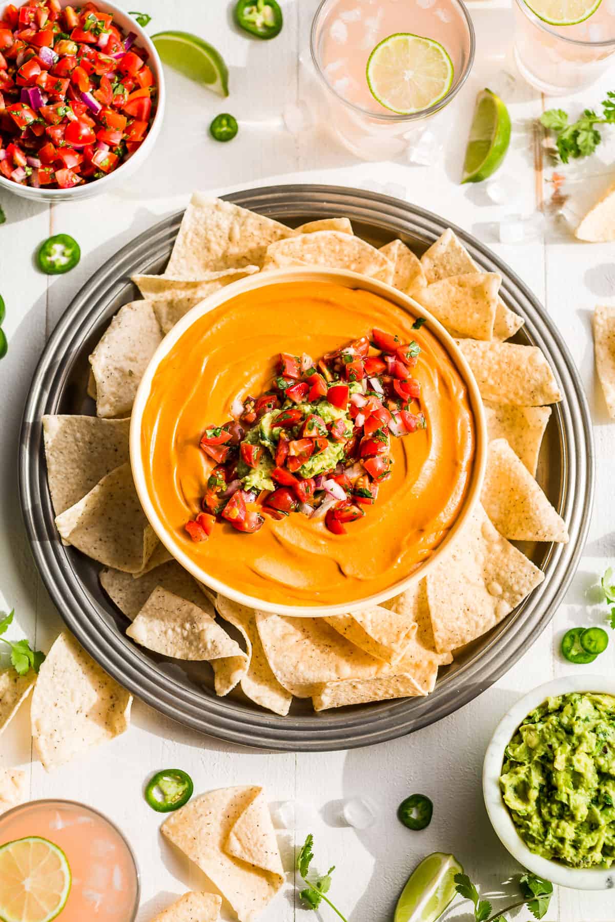 Straight down view of Best Vegan Queso topped with fresh salsa & guacamole surrounded by chips with bowls of fresh salsa and guacmole.
