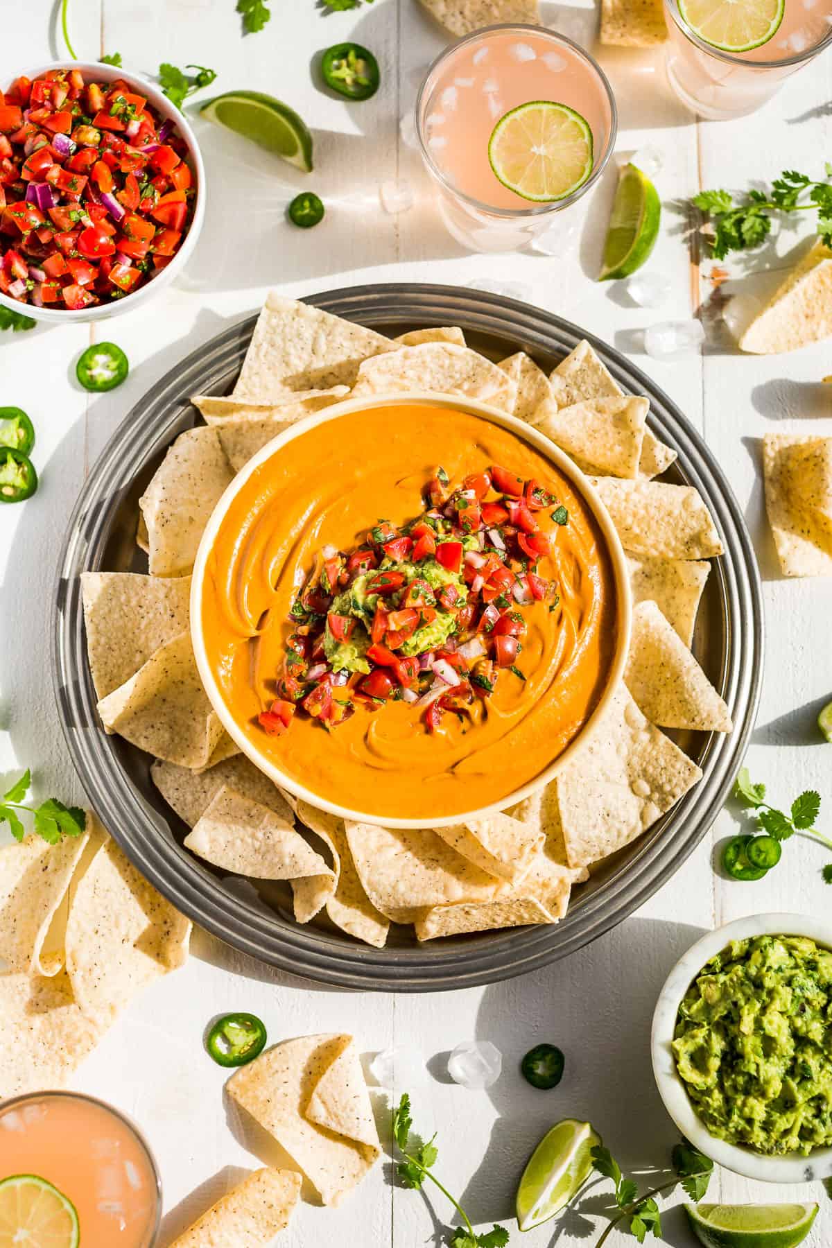 Best Vegan Queso topped with fresh salsa and guacamole surrounded by chips and small bowls of salsa and guacamole.