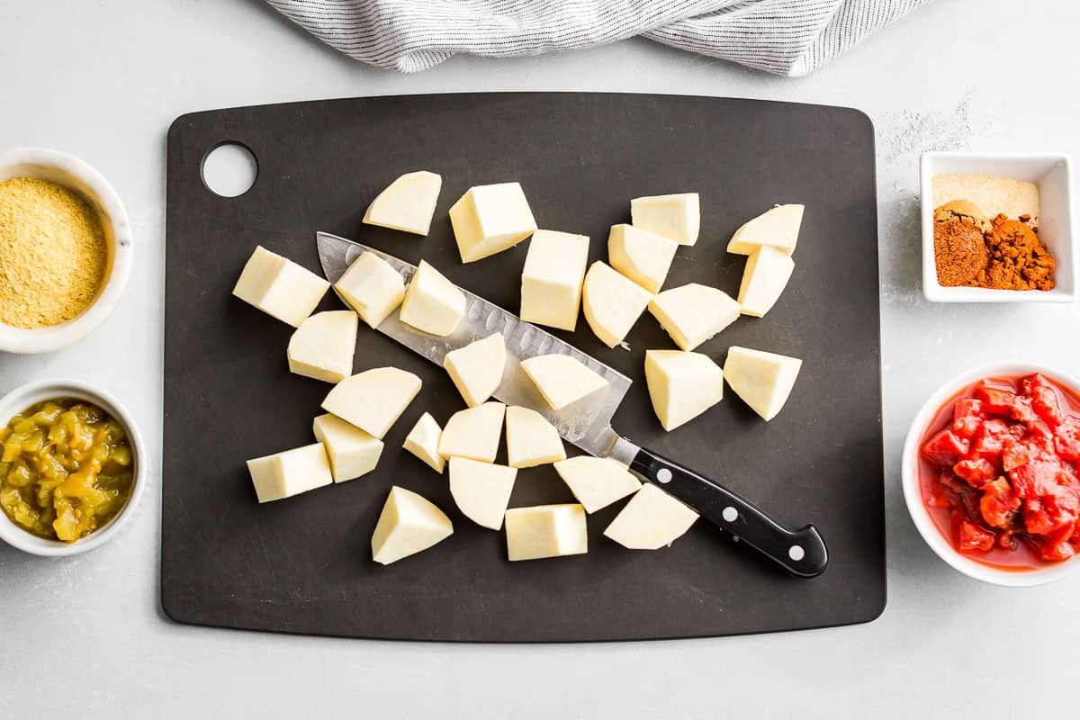 Cut up white sweet potatoes on a black cutting board with diced tomatoes and green chilies on the side.