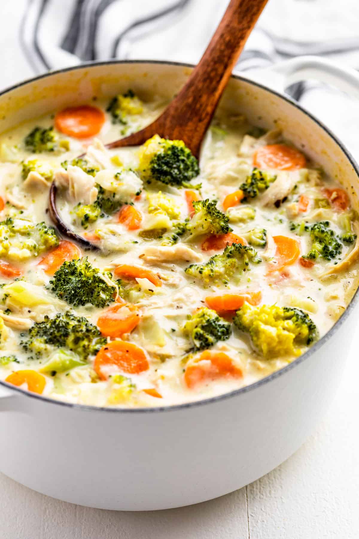 Side view of Chicken Broccoli Soup in a white pot with a wood ladle.