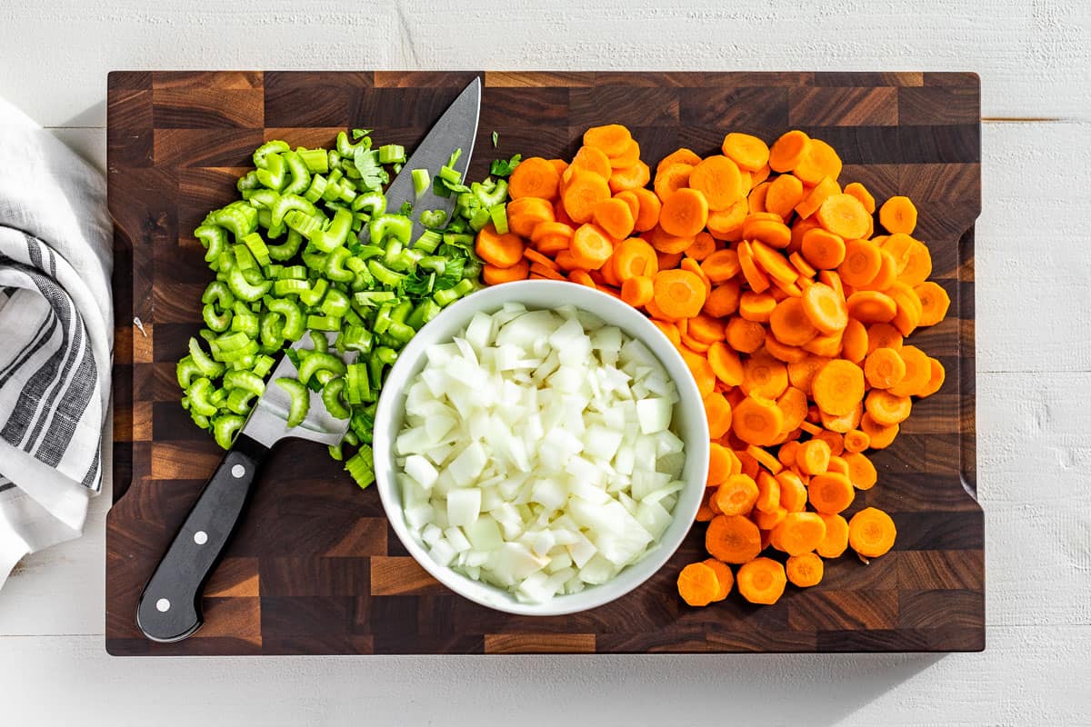 Chopped onions, celery, and carrots on a wood cutting board.