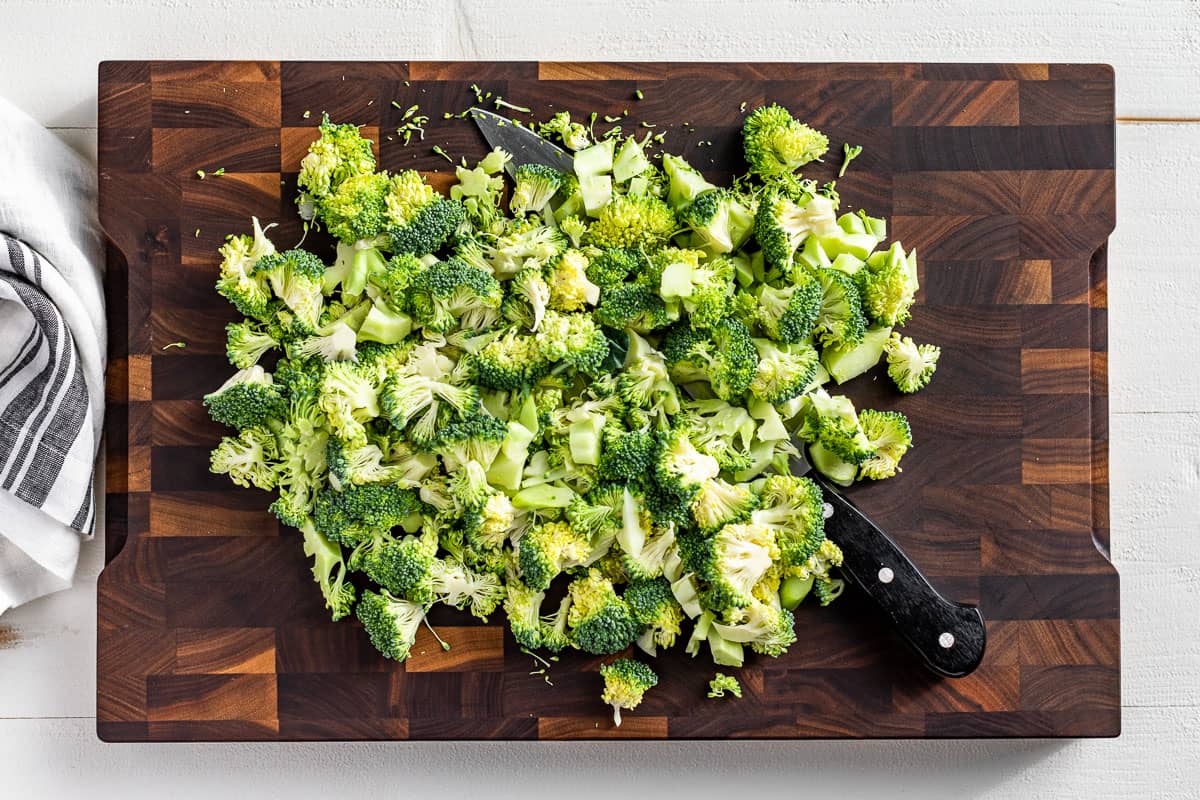 Chopped up broccoli florets on a wood cutting board.