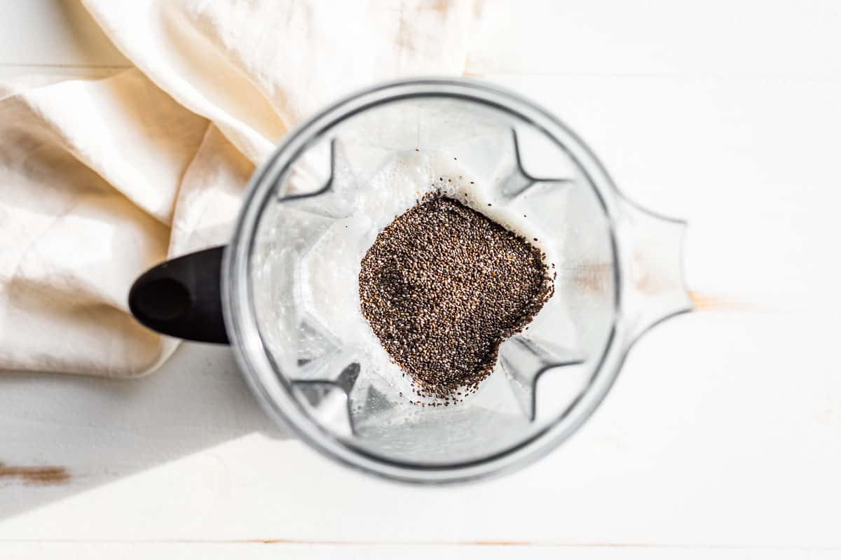 The chia seeds being added to the creamy coconut mixture in the blender.