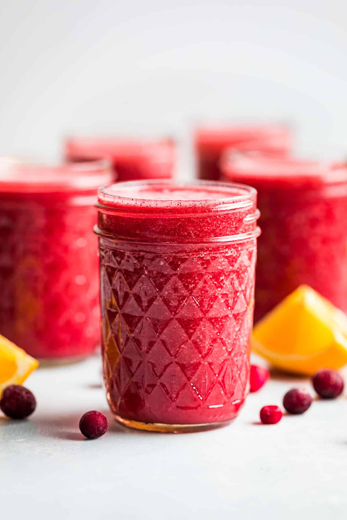 5 glasses full of Cranberry Orange Smoothie with frozen cranberries and orange wedges place around them.