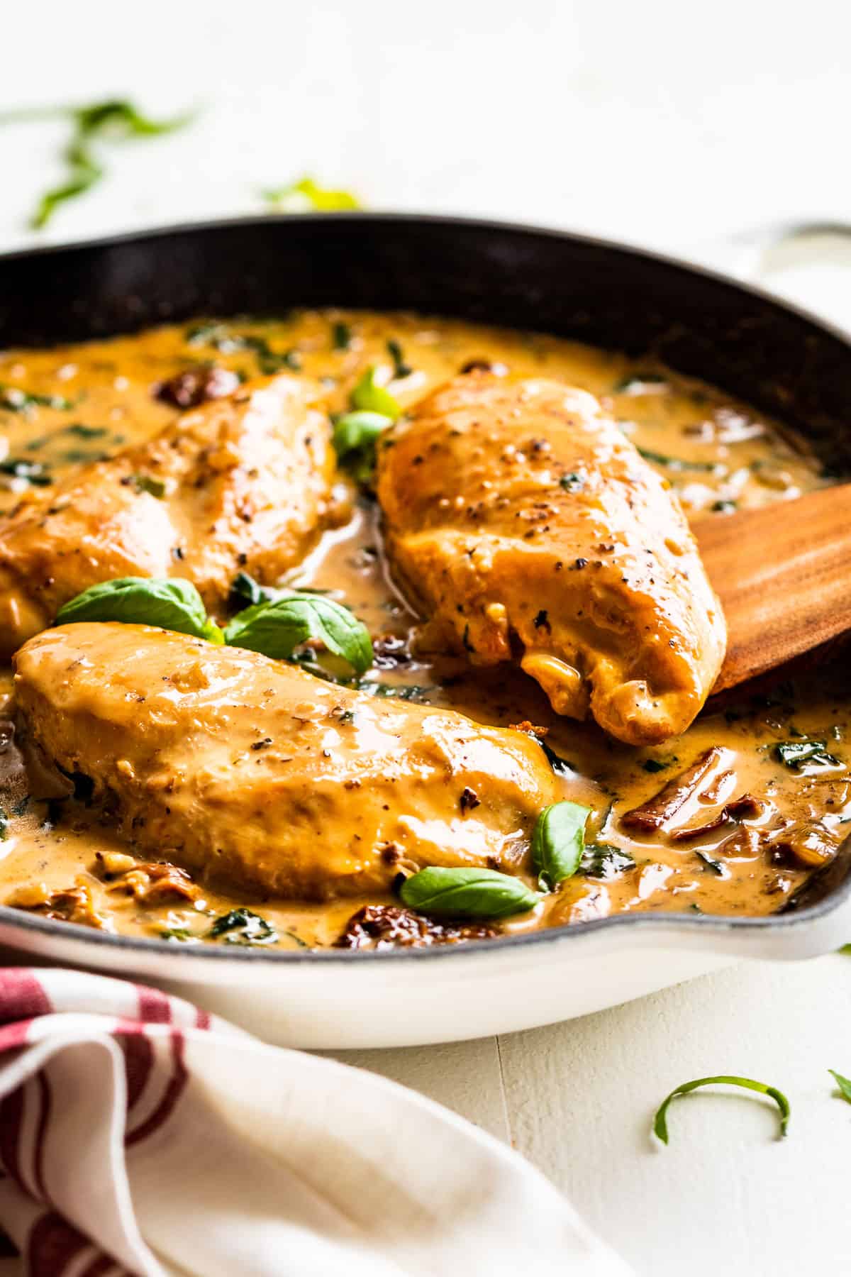 Creamy Tuscan Chicken in a white skillet with basil leaves on top.