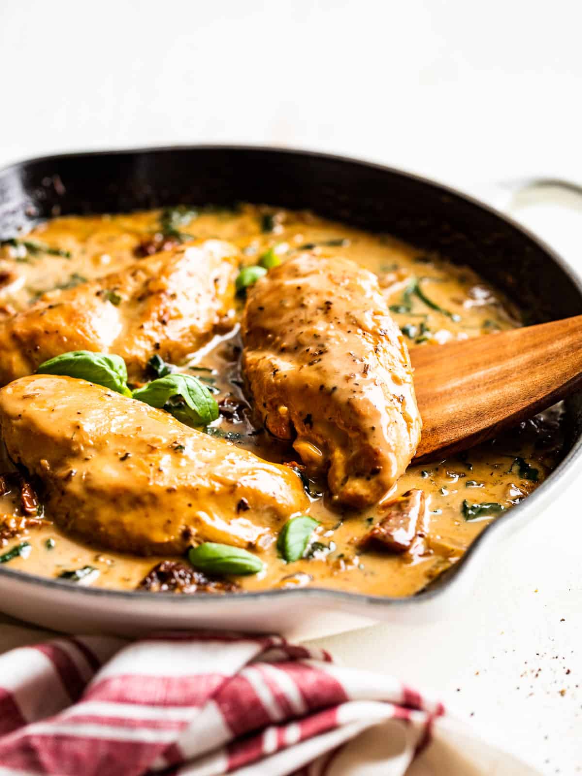 Creamy Tuscan Chicken in a white skillet with a red and white striped linen next to it.