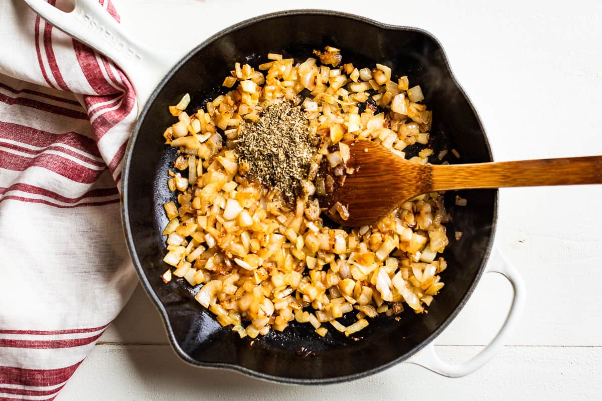 The second step of the recipe sautéing the onions and garlic in a white skillet.