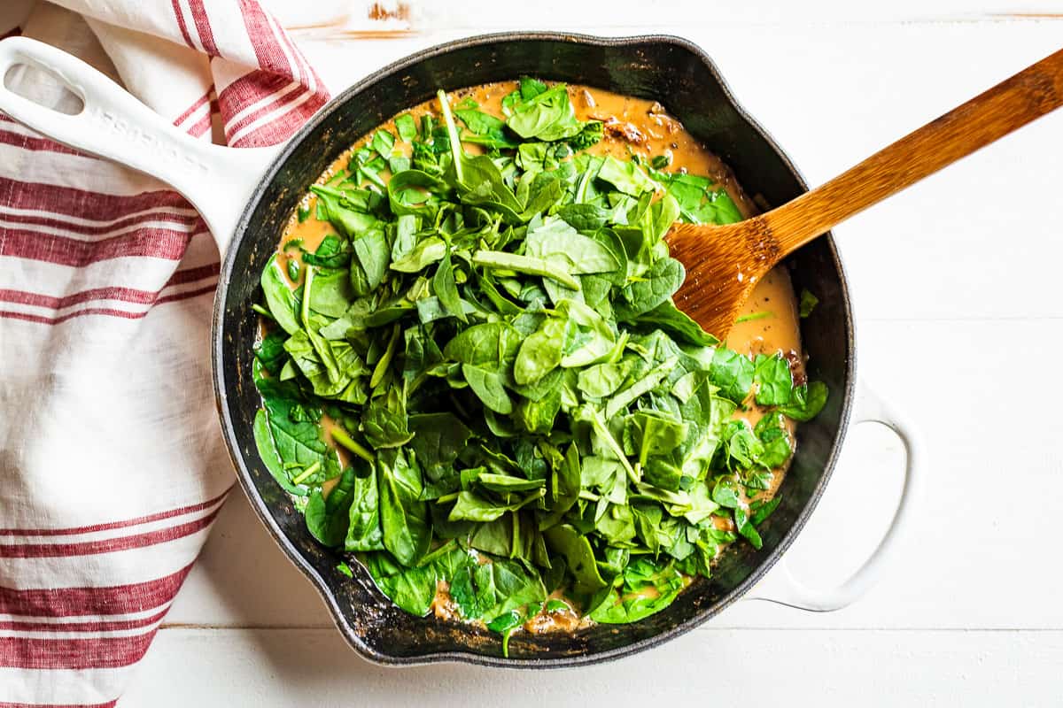 The final step of adding the chopped spinach to the Creamy Tuscan Chicken.