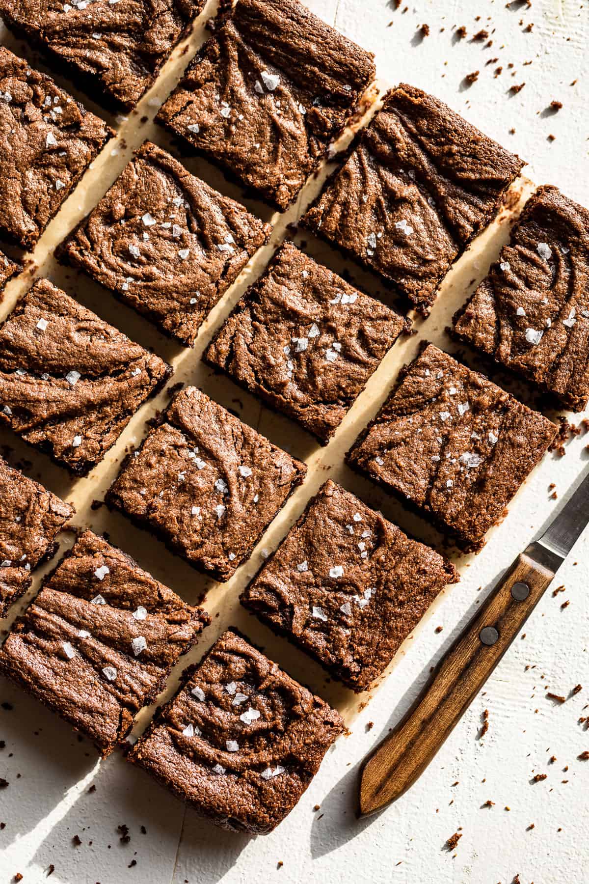 Batch of flourless brownies on a white background sliced and sprinkled with flaked sea salt.