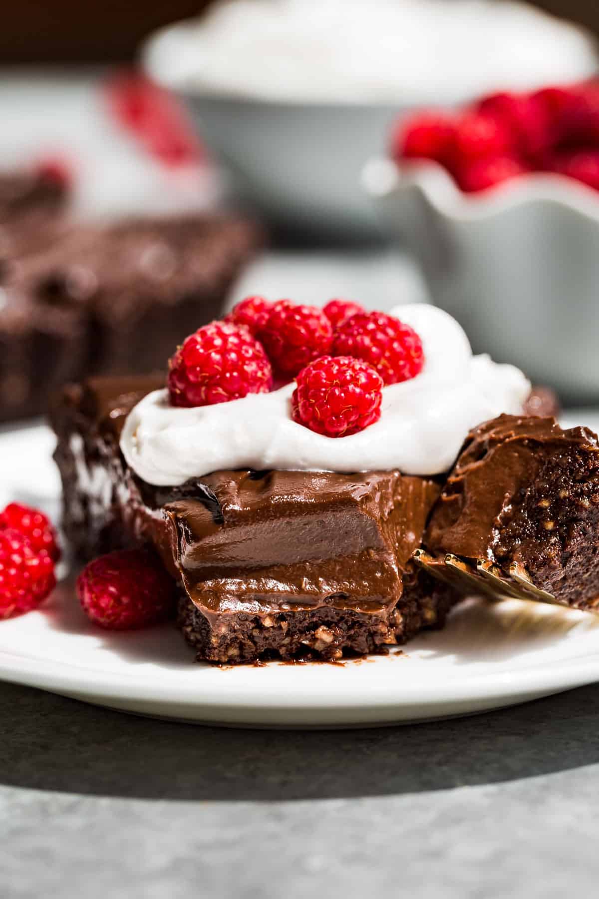 A slice of Healthy Chocolate Tart on a white plate topped with whipped cream and raspberries.