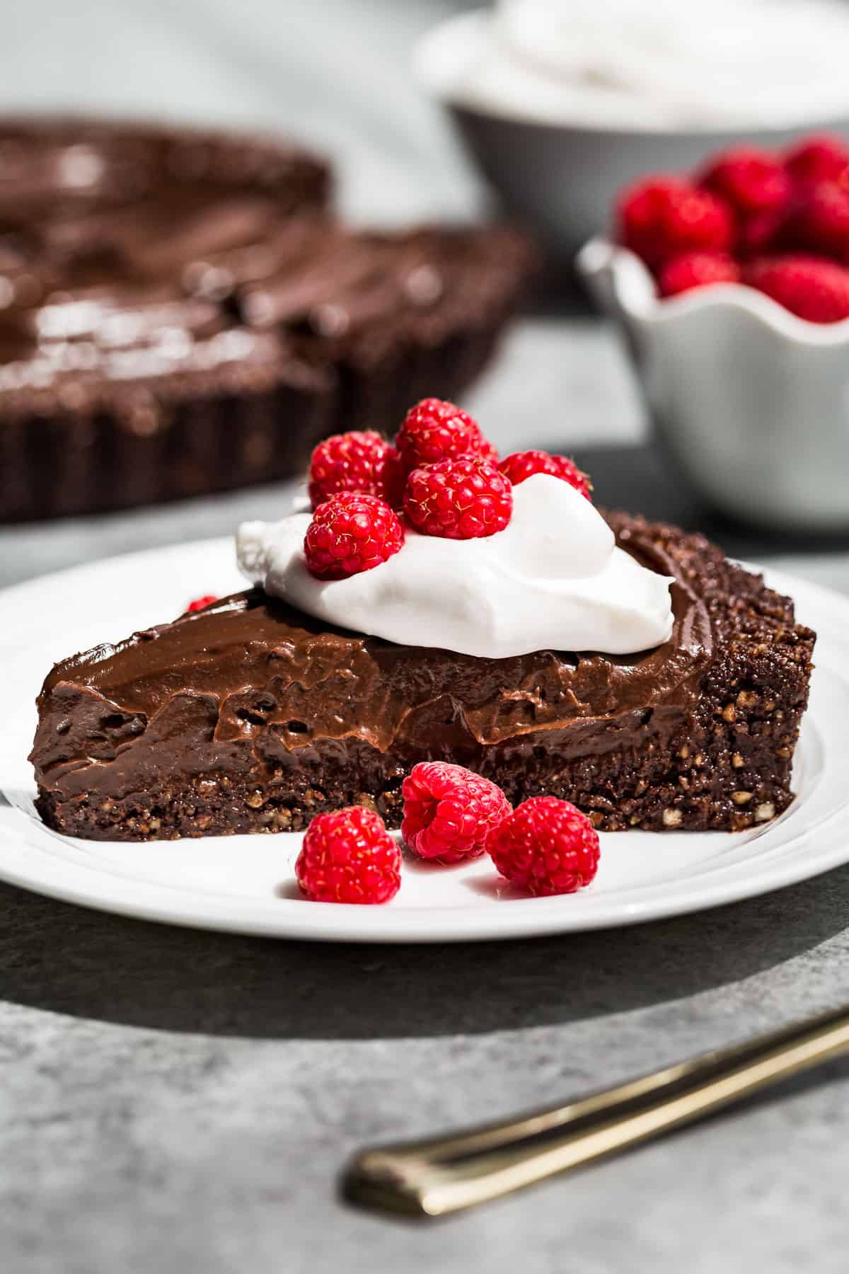 A side view of a slice of Chocolate Tart topped with whipped cream and raspberries.