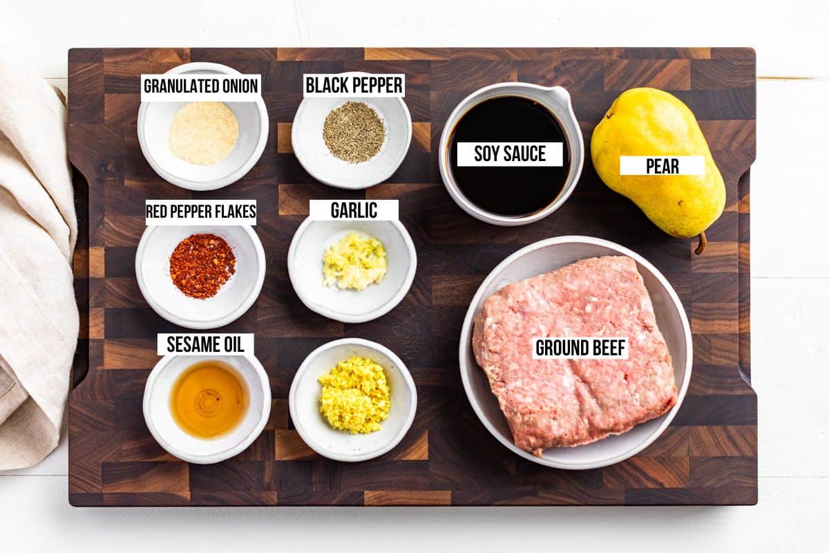 All the ingredients for the Korean Ground Beef in measuring bowls on a wood cutting board, ground beef, ginger, garlic, sesame oil, soy sauce, and a pear.