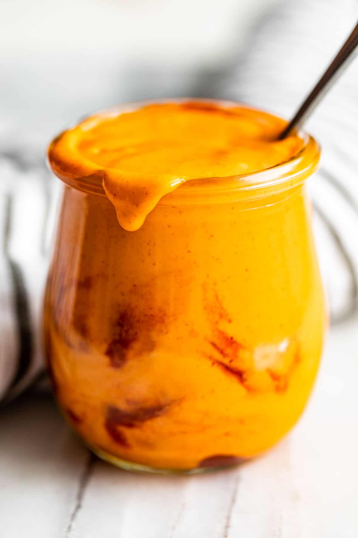 Sriracha swirled into Sriracha Mayo in a clear glass jar with a little bit spilling over the top.