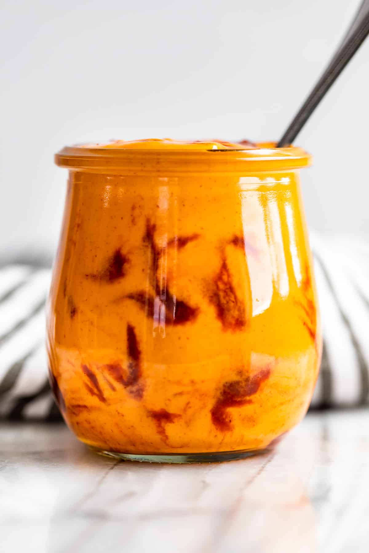 Sriracha swirled on a glass jar filled with Sriracha Mayo with a silver spoon in it.