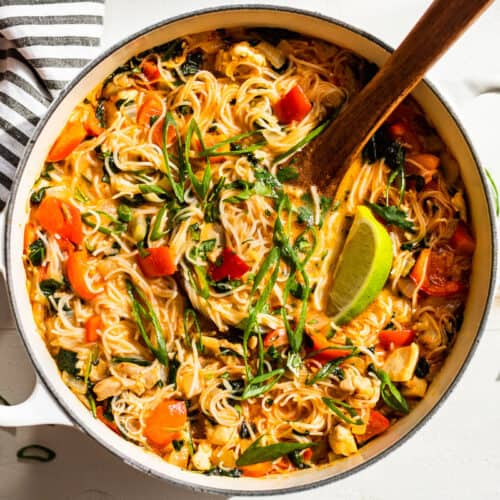 Finished Thai Curry Noodle Soup with a wooden ladle on a white background.