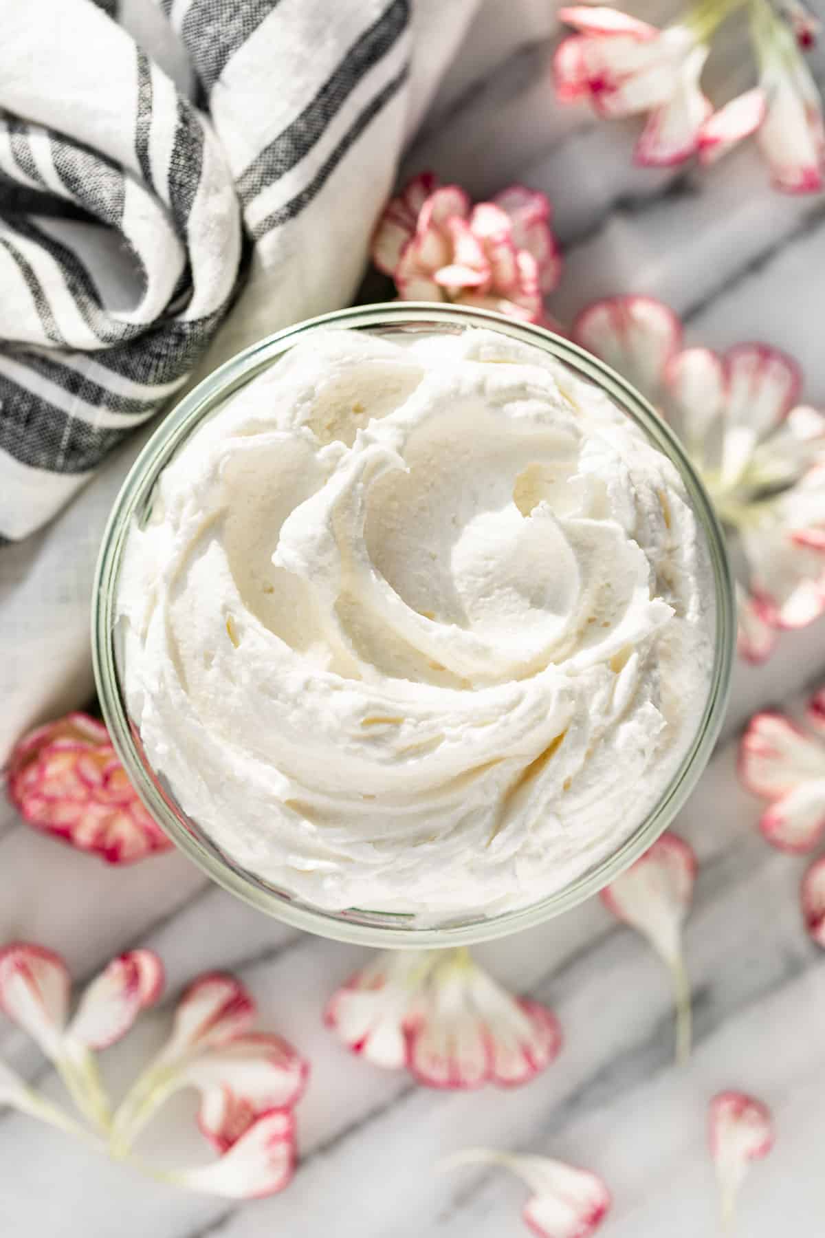 Straight down view of Whipped Body Butter in a glass jar with pink and white flower petals surrounding it.