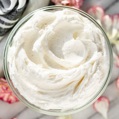 Whipped Body Butter in a glass jar with a grey linen in the background and flower petals surrounding it.