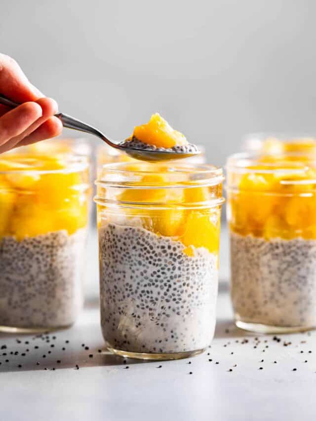 A spoonful of Cream Coconut Pudding with a mango chunk being lifted out of the mason jar.
