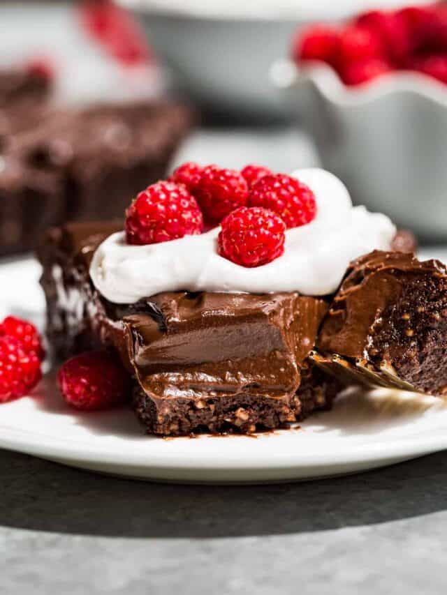 A slice of Healthy Chocolate Tart on a white plate topped with whipped cream and raspberries.