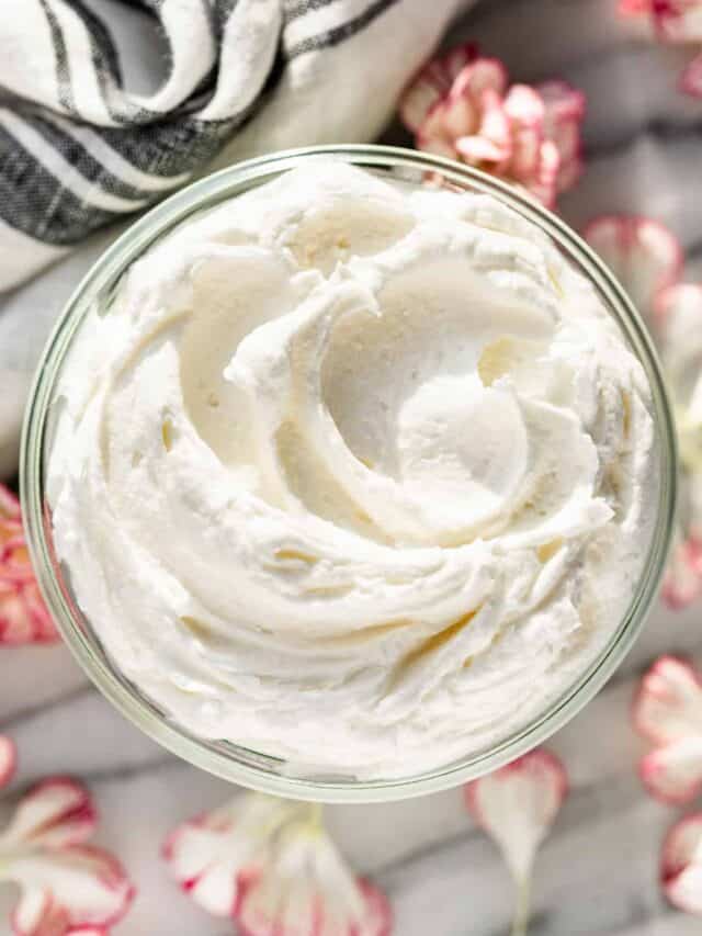 Straight down view of Whipped Body Butter in a glass jar with a grey linen in the background and flower petals surrounding it.