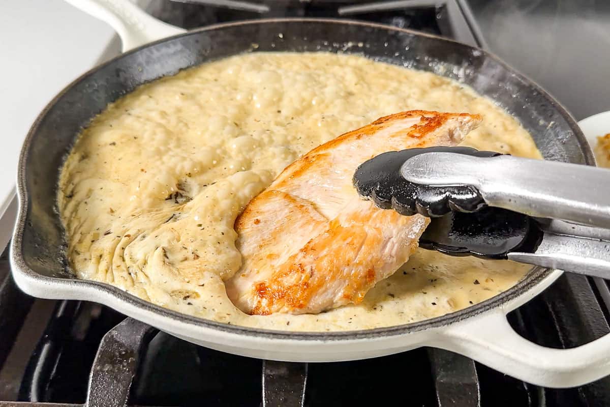 Adding the browned chicken breasts back to the creamy Tuscan sauce.