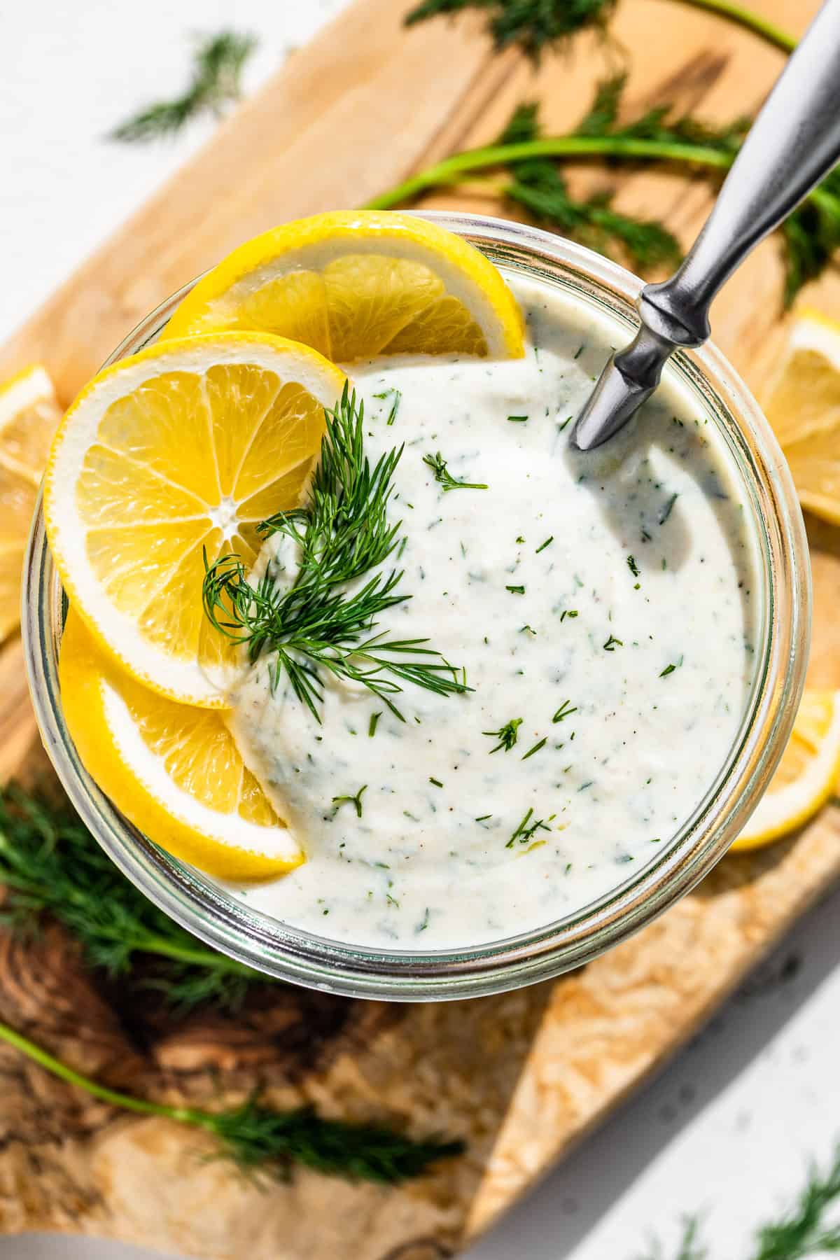 Straight down view of Greek Yogurt Dressing in a clear glass jar topped with lemon slices and a sprig of dill.