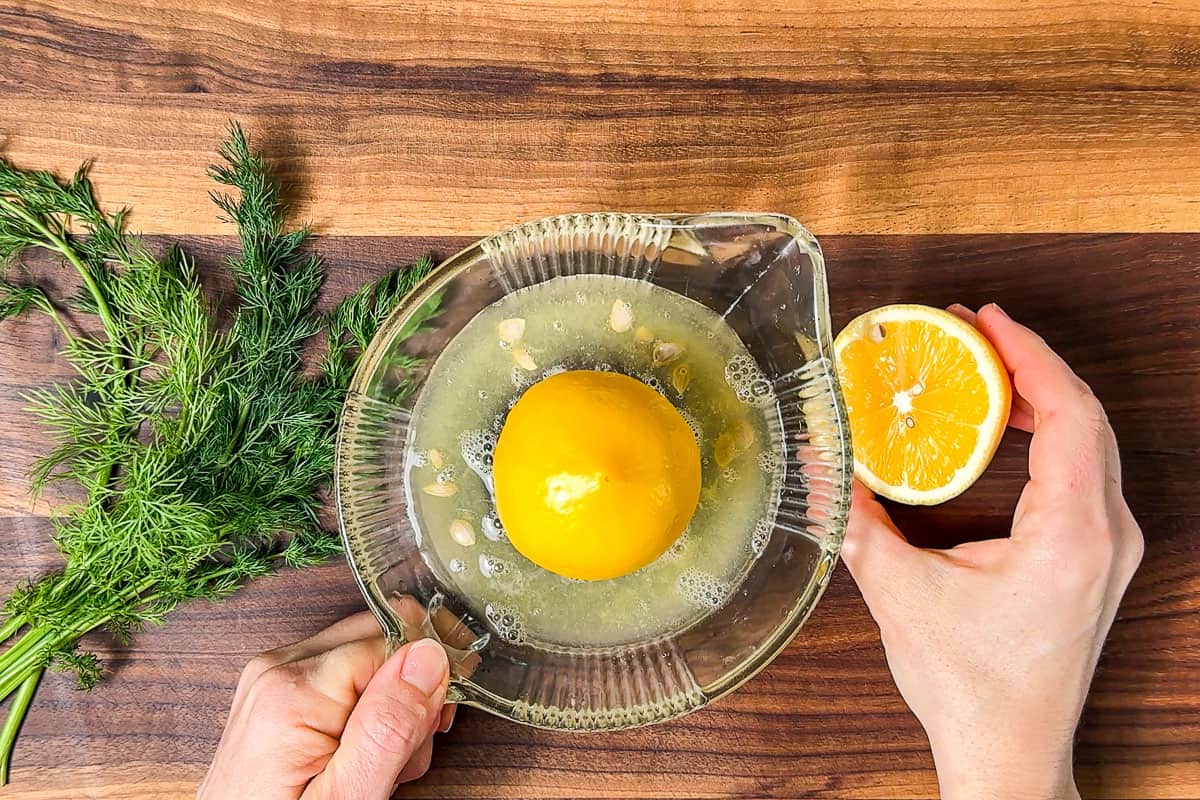 Juicing a lemon on a glass reamer on a wood cutting board.