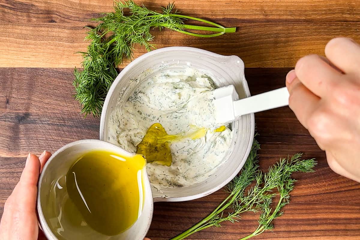 Adding the olive oil to the Greek Yogurt dressing in a small pottery bowl.