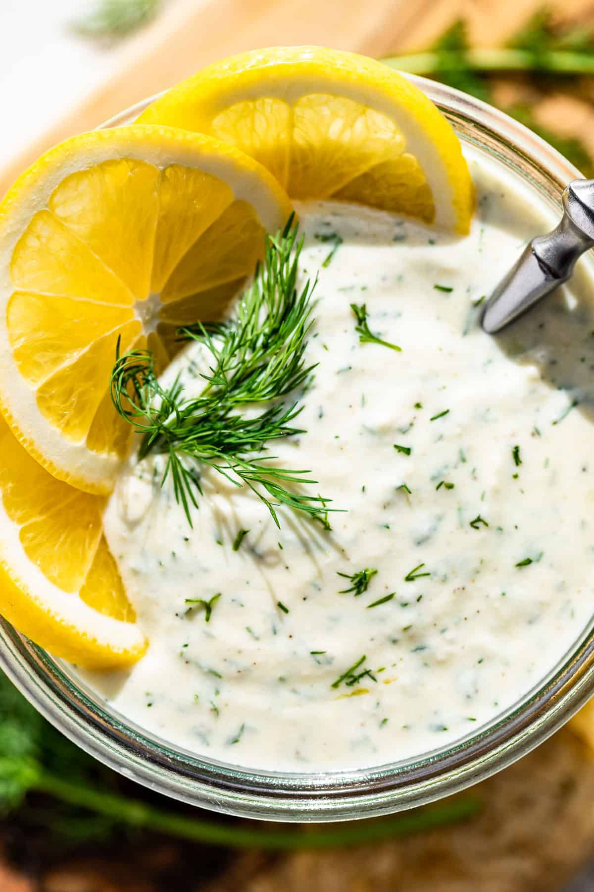 Straight down close up view of Greek Yogurt Dressing topped with lemon slices and chopped dill.