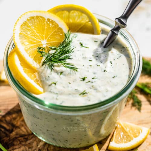 Side view of finished Greek Yogurt Dressing in a glass jar topped with lemon slices and a sprig of dill.