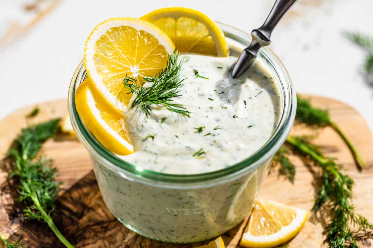 Side view of finished Greek Yogurt Dressing in a glass jar topped with lemon slices and a sprig of dill.