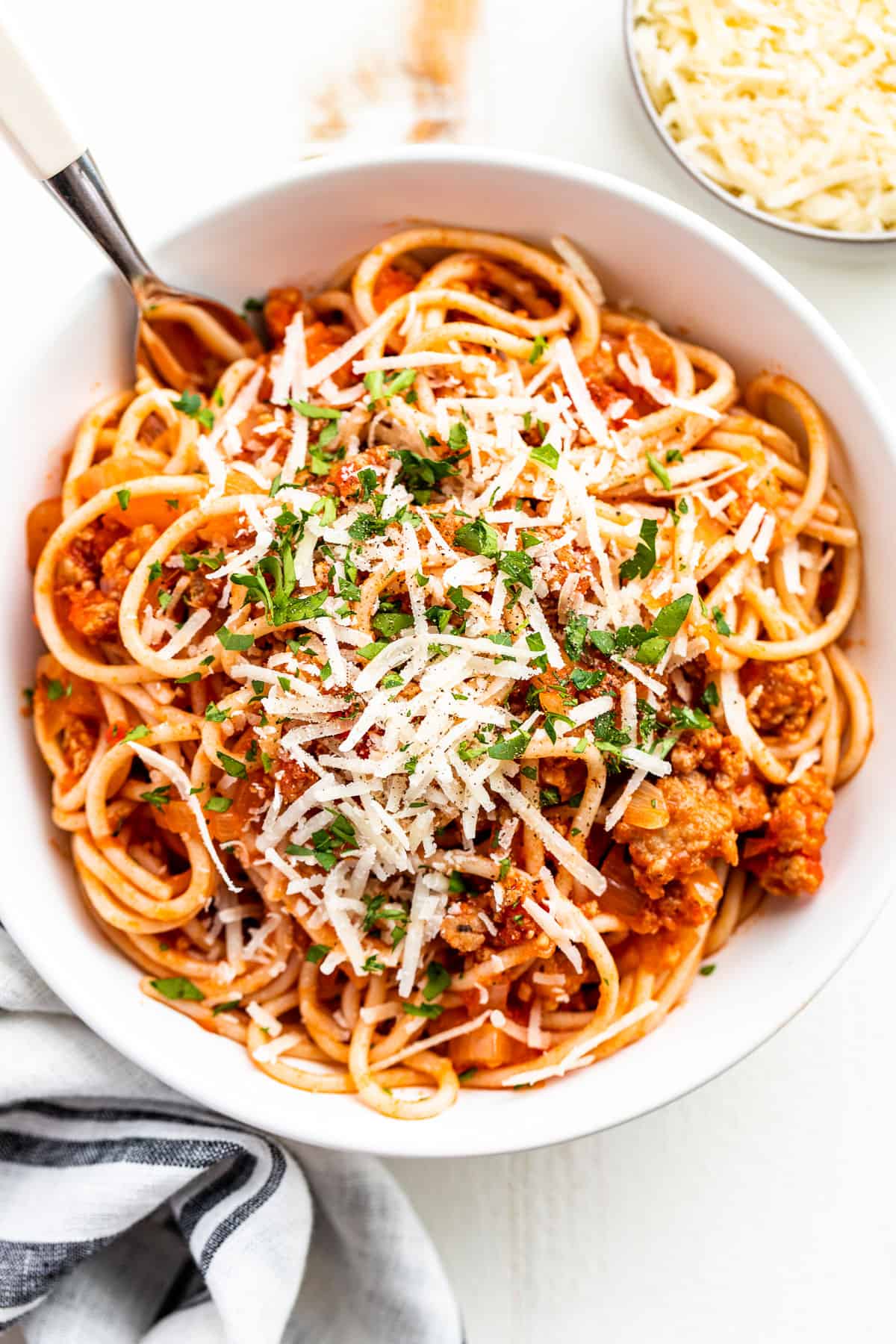 Straight down view of spaghetti in a white bowl sprinkled with parmesan and chopped parsley.