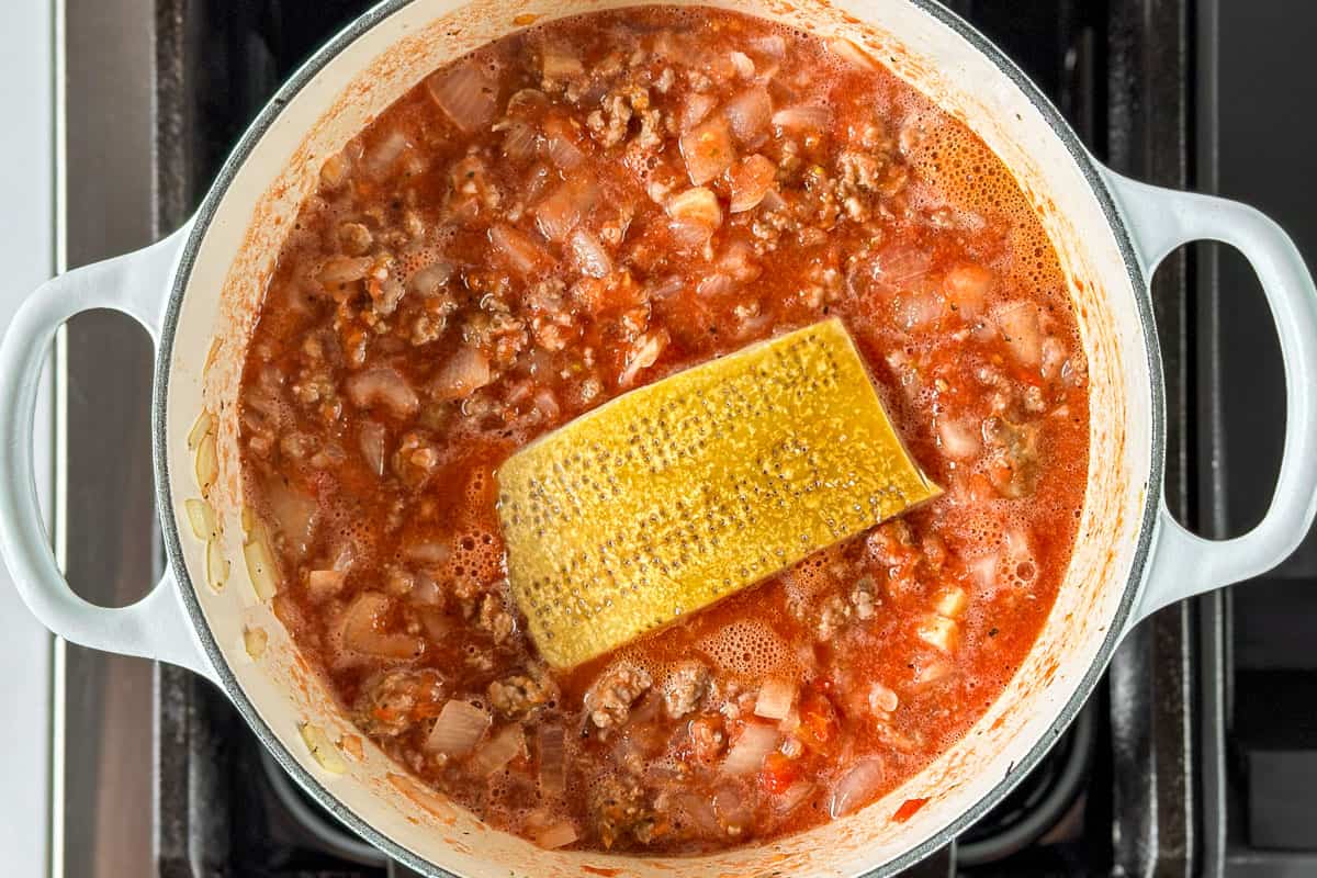 Adding the blended canned tomatoes to the sausage mixture along with the parmesan rind.