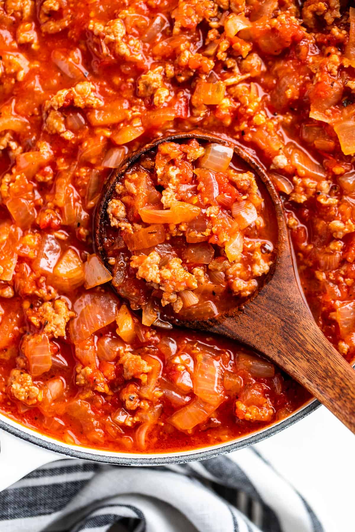 Straight down view of Spaghetti Sauce in a white pot with a wood ladle.