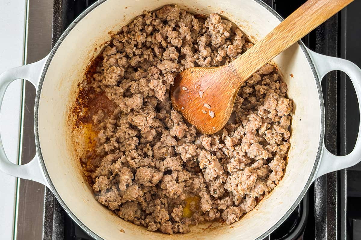 Sautéing Italian sausage in a large white pot with a wooden spoon.