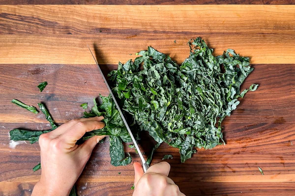 Thinly slicing the kale on a wood cutting board.