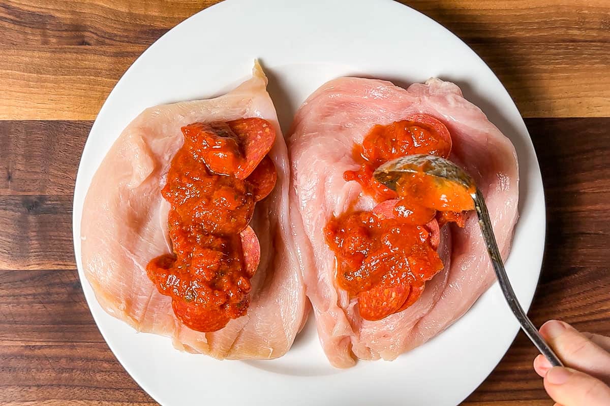 Spooning tomato sauce onto the pepperoni slices.