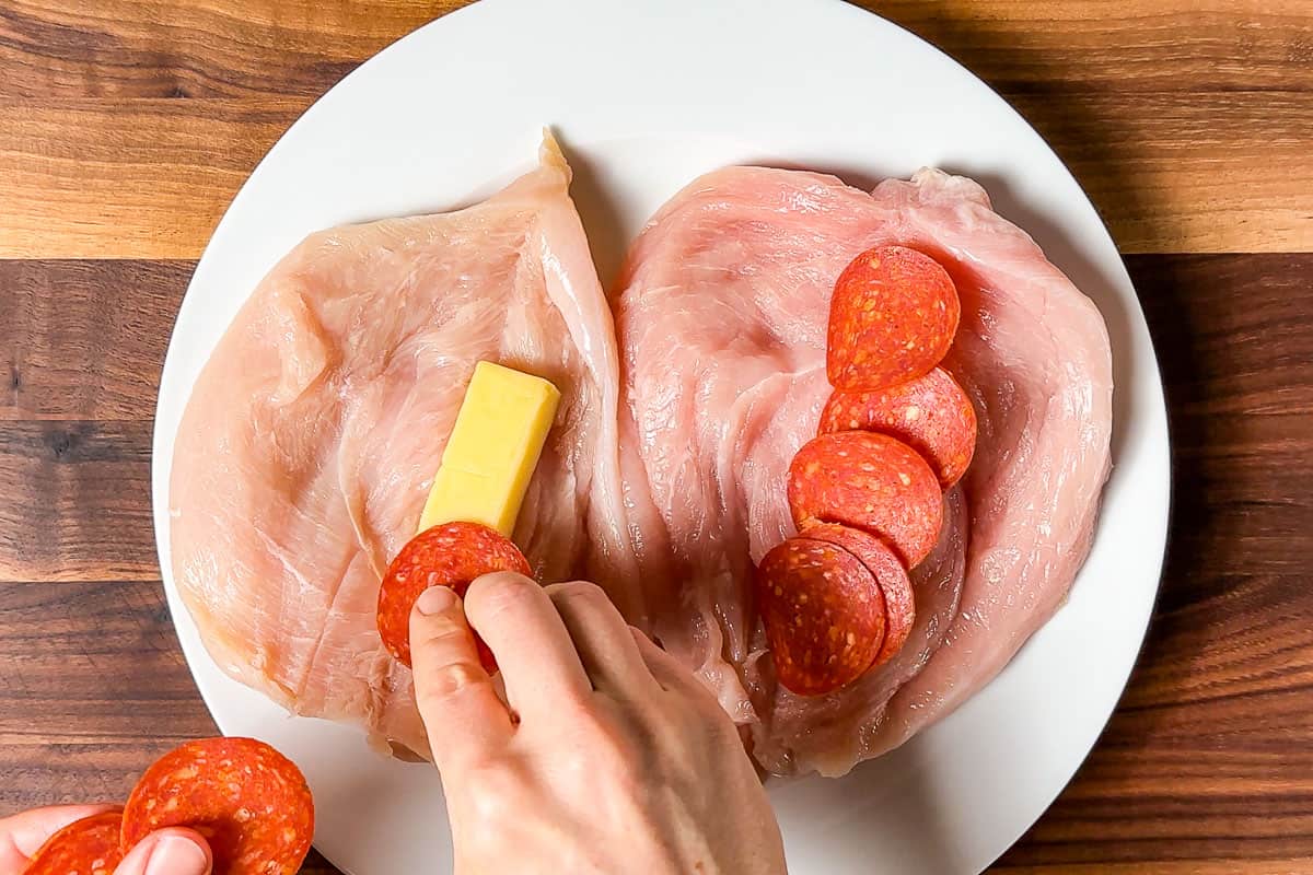 Layering sliced mozzarella and pepperoni onto the butterflied chicken breasts.