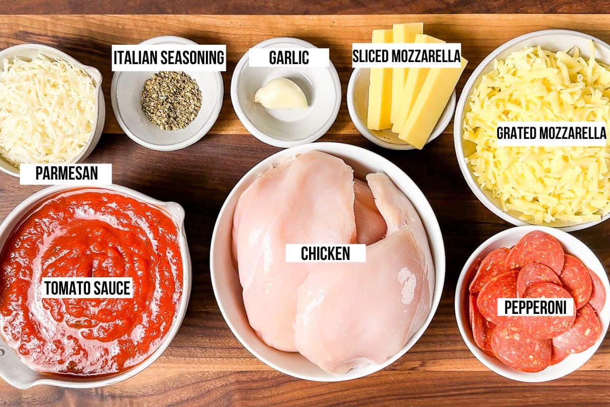 Tomato sauce, chicken breasts, pepperoni, mozzarella, parmesan, garlic, and Italian seasoning on a wood cutting board.