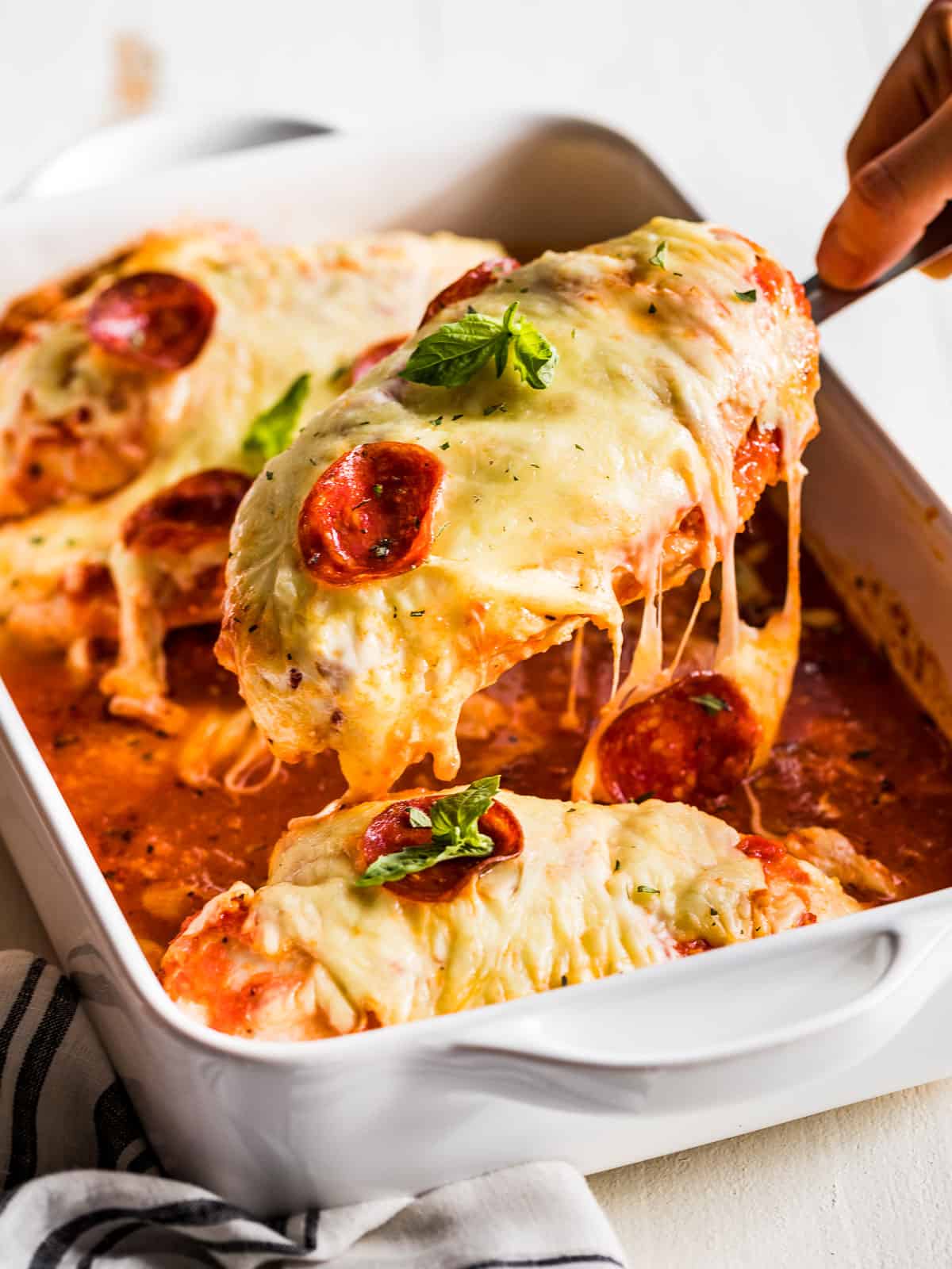 Pizza Chicken being lifted out of the dish with a wood spatula.