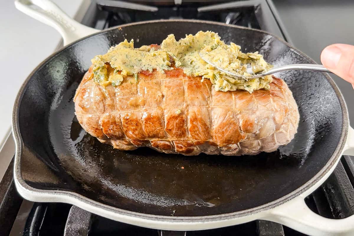 Spreading the garlic herb butter over the top of the seared roast.