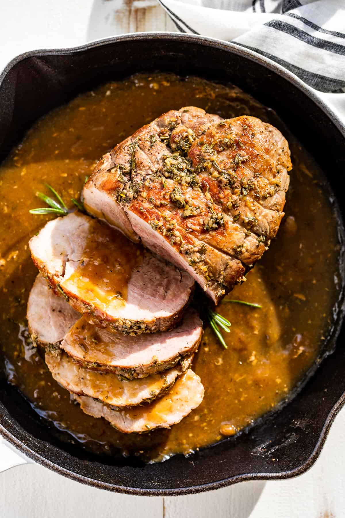 Straight down view of Pork Sirloin Roast in a white skillet with half of it sliced.