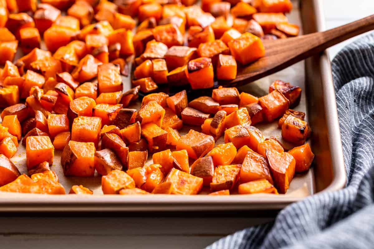 Roasted Sweet Potatoes on a baking sheet with a wood spatula.