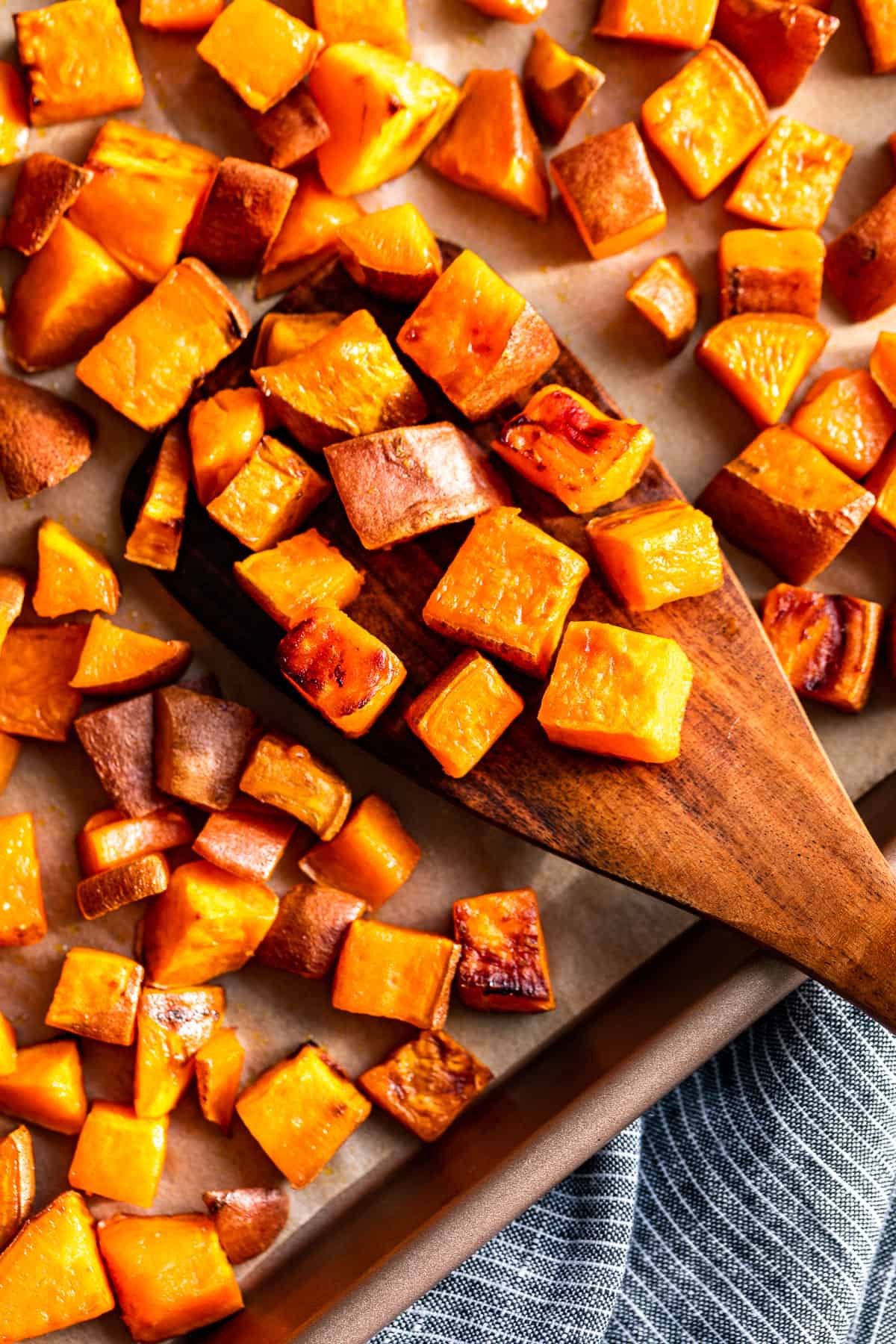 Cubed Roasted Sweet Potatoes on a baking sheet with a wood spatula scooping some off.