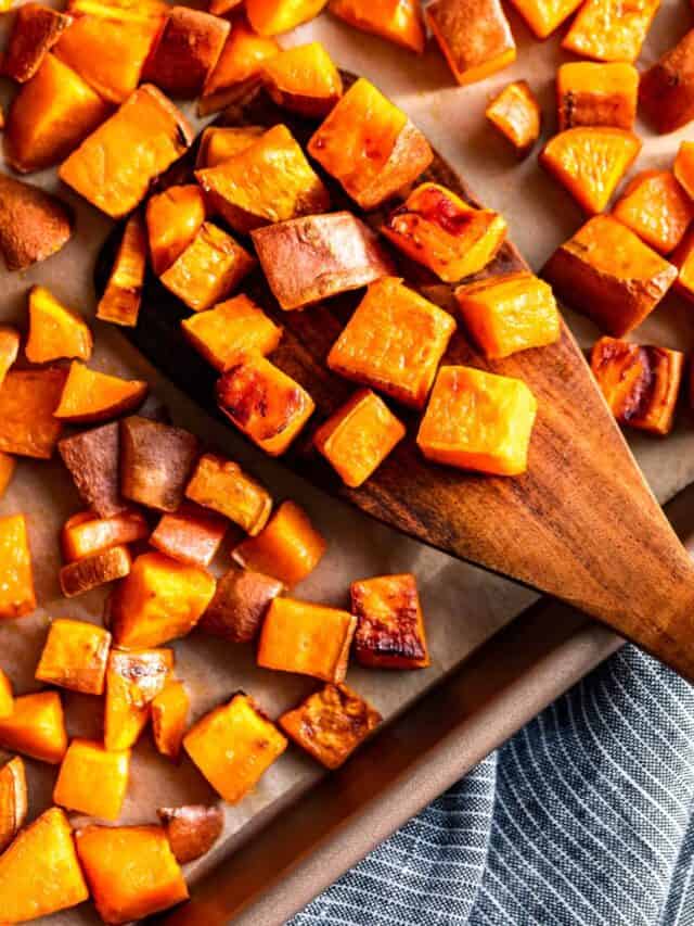 Cubed Roasted Sweet Potatoes on a baking sheet with a wood spatula scooping some off.
