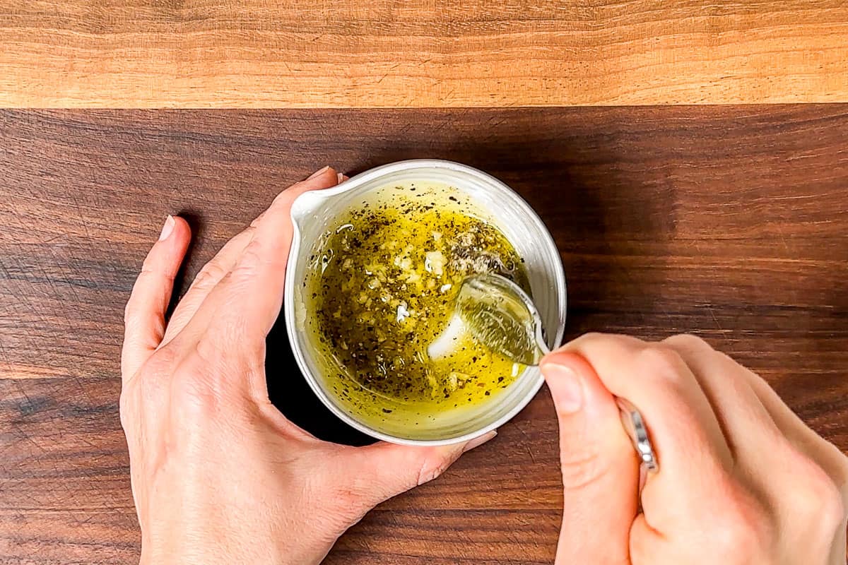 Mixing together the olive oil, garlic, sea salt, and pepper in a small pottery bowl.