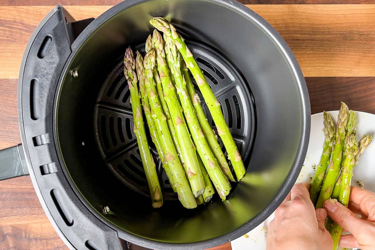 Adding the olive oil coated asparagus to the air fryer.